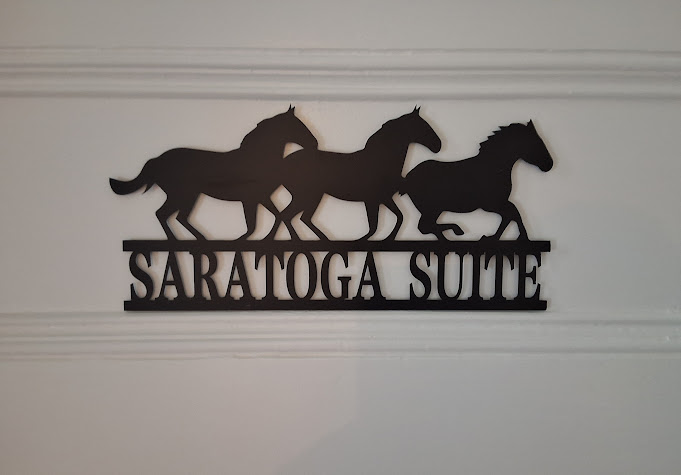 A laser-cut metal sign featuring three running horses and the words Saratoga Suite adorn a white door.