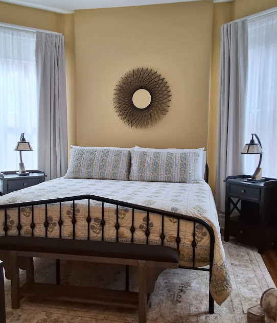 Tranquil bedroom with natural light, a king-size metal bed flanked by matching nightstands with lamps, hardwood floors, and area rug.