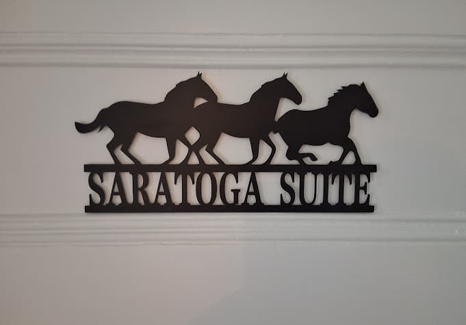 A laser-cut metal sign featuring three running horses and the words Saratoga Suite adorn a white door.