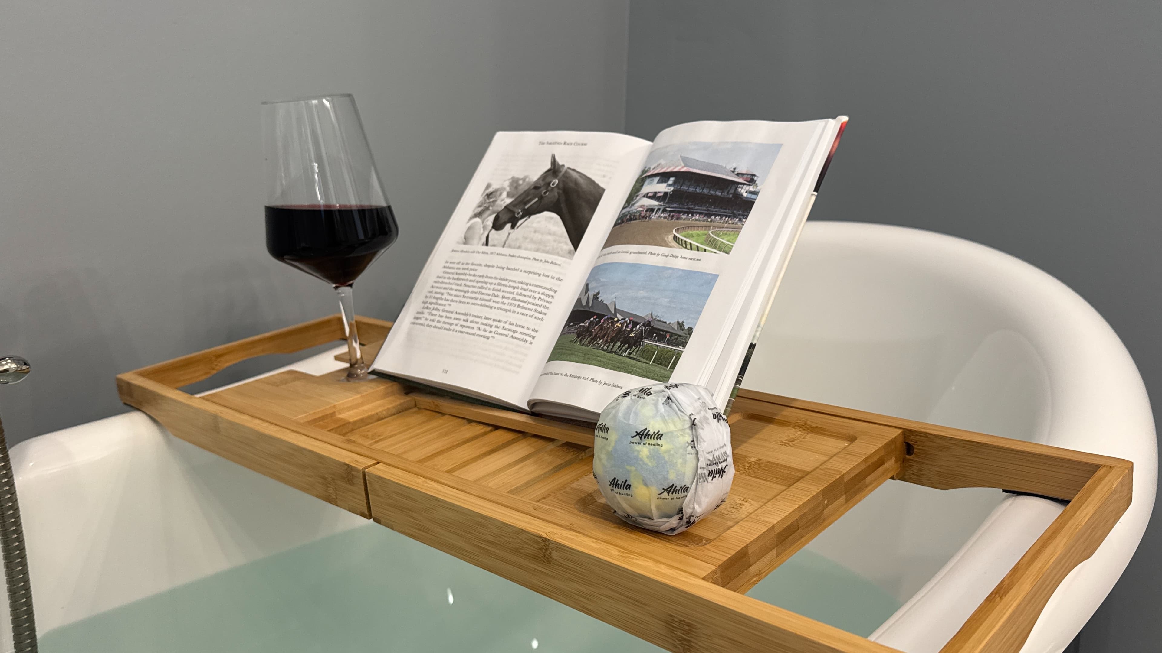 A tub reading table with a book, glass of wine and a bath bomb