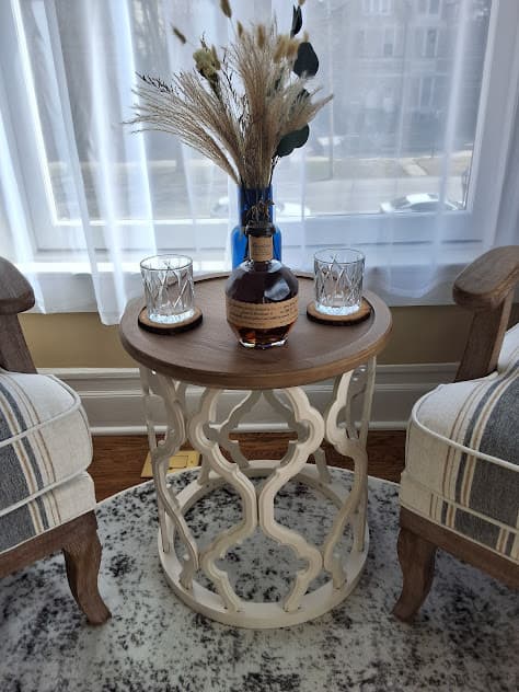Sitting area with end table flanked by upholstered chairs in front of a window with white sheer curtain.