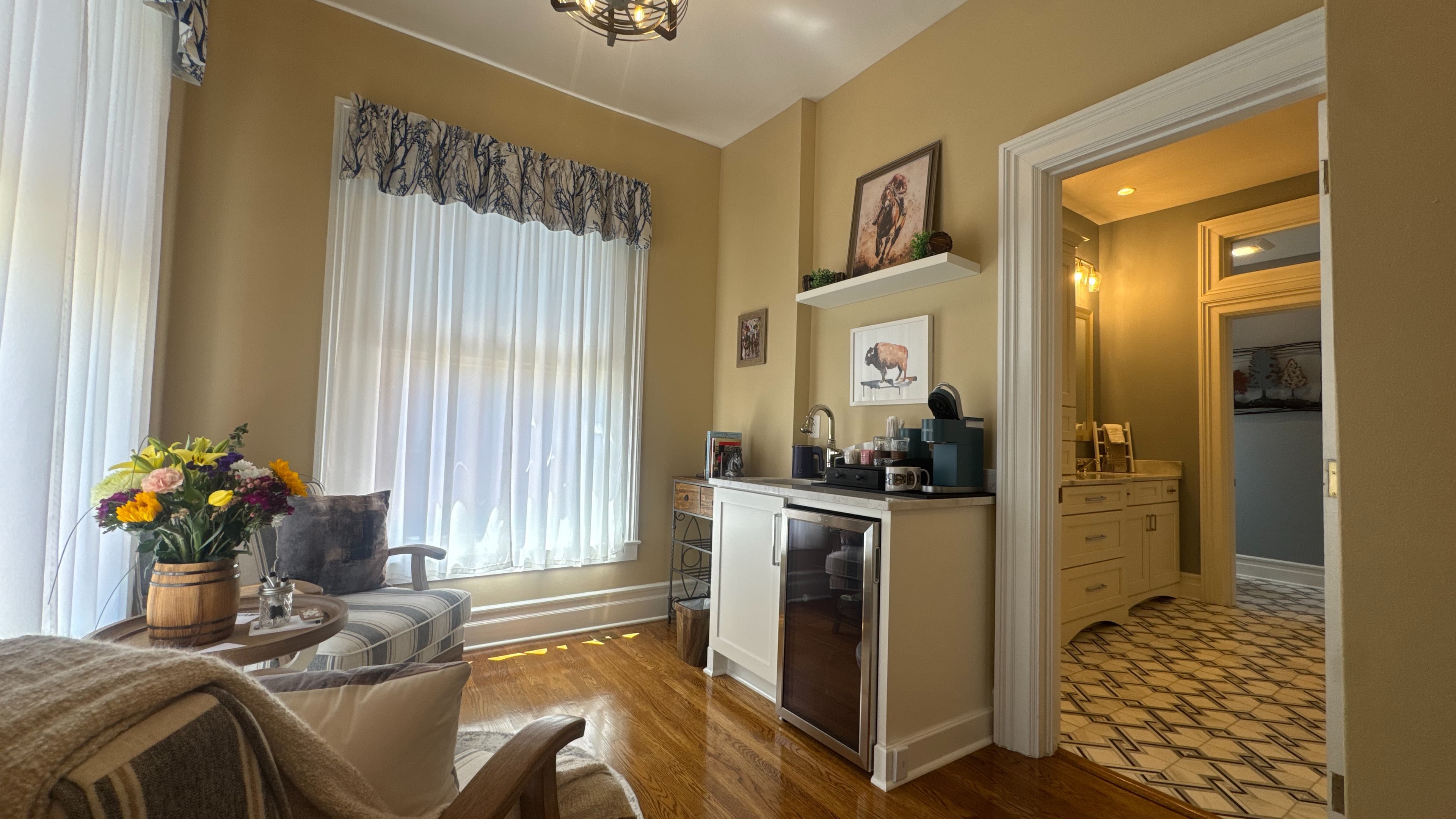 Sink area in morning room with coffee maker, mugs, and mini-fridge next to book cart.
