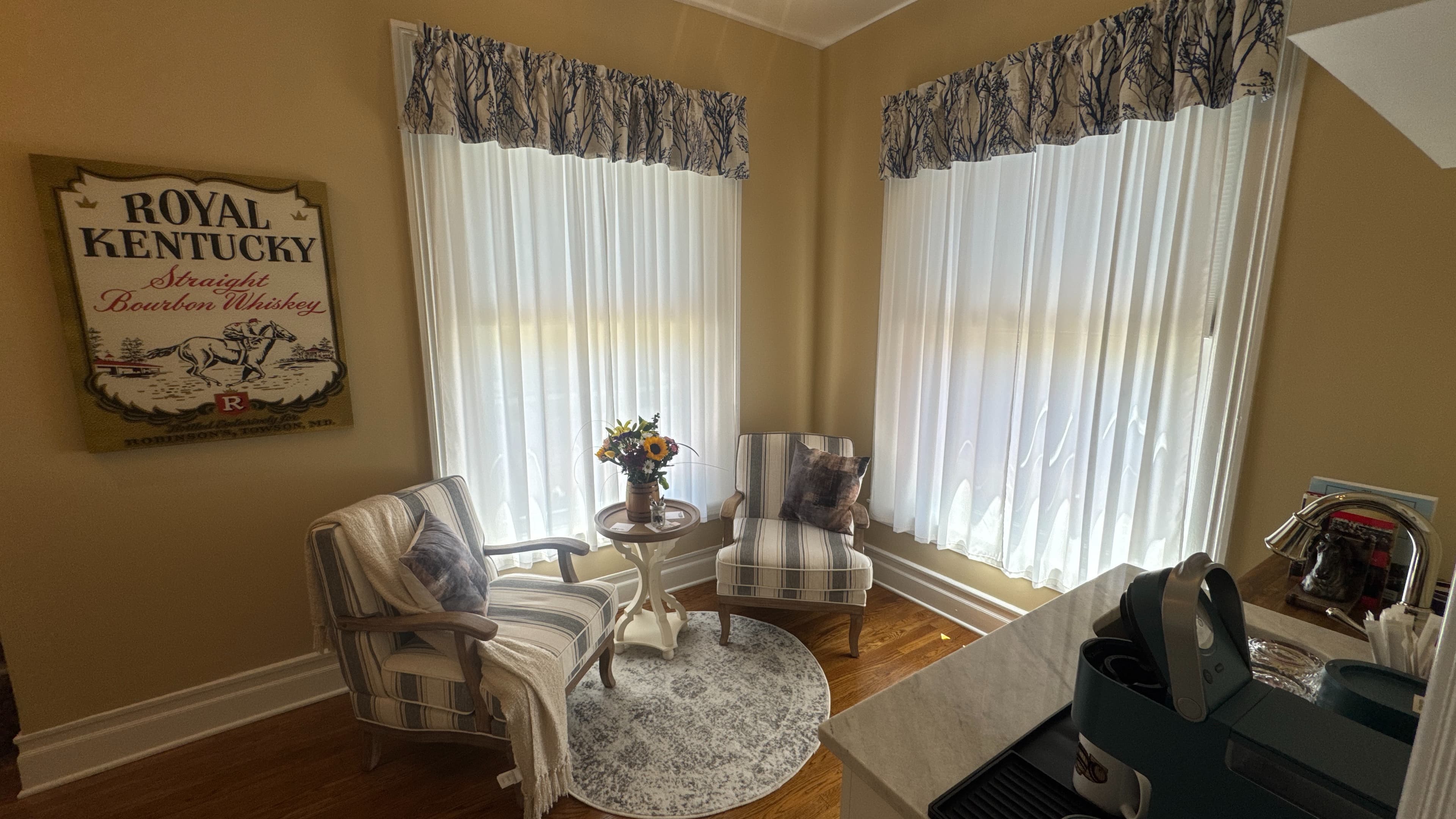 Sitting area with end table flanked by upholstered chairs in front of a window with white sheer curtain.