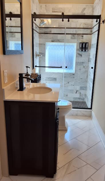 Gleaming, modern bathroom with vanity & sink, toilet, and glass-enclosed tiled shower.