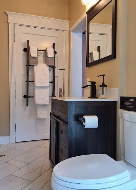 Private bathroom with toilet, sink with vanity, tiled floor, and plush white towels hanging on door-mounted ladder rack.