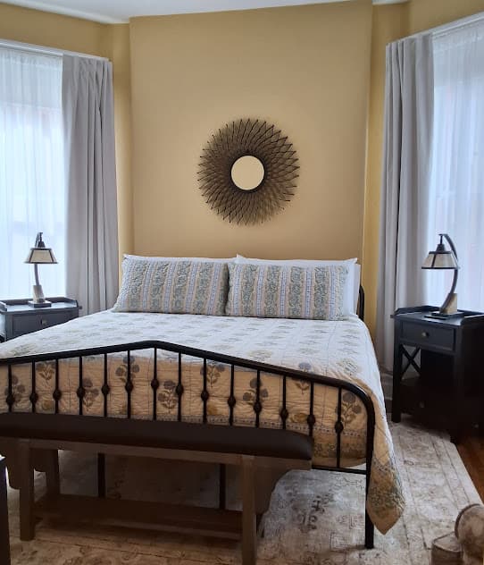 Tranquil bedroom with natural light, a king-size metal bed flanked by matching nightstands with lamps, hardwood floors, and area rug.