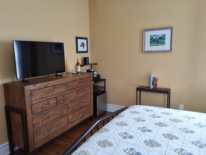 Wooden dresser topped with flat-screen TV next to wall opposite the king-size bed.