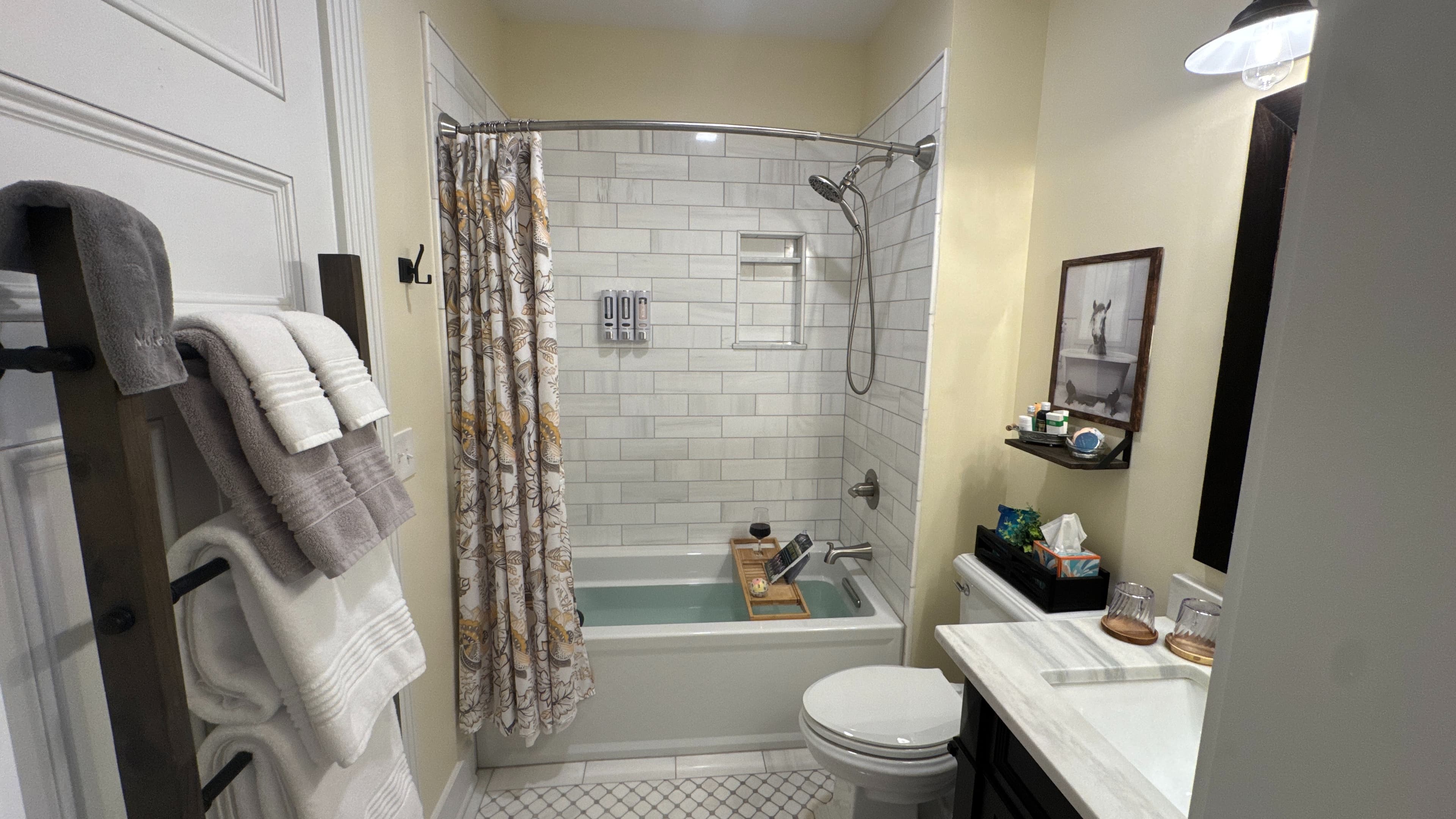 Cozy bathroom with a filled tub, bath tray, wine glass, book, and floral shower curtain