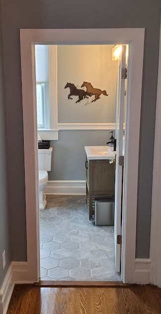 A doorway frames a view into a bathroom with a toilet, vanity, and horse artwork on the wall.