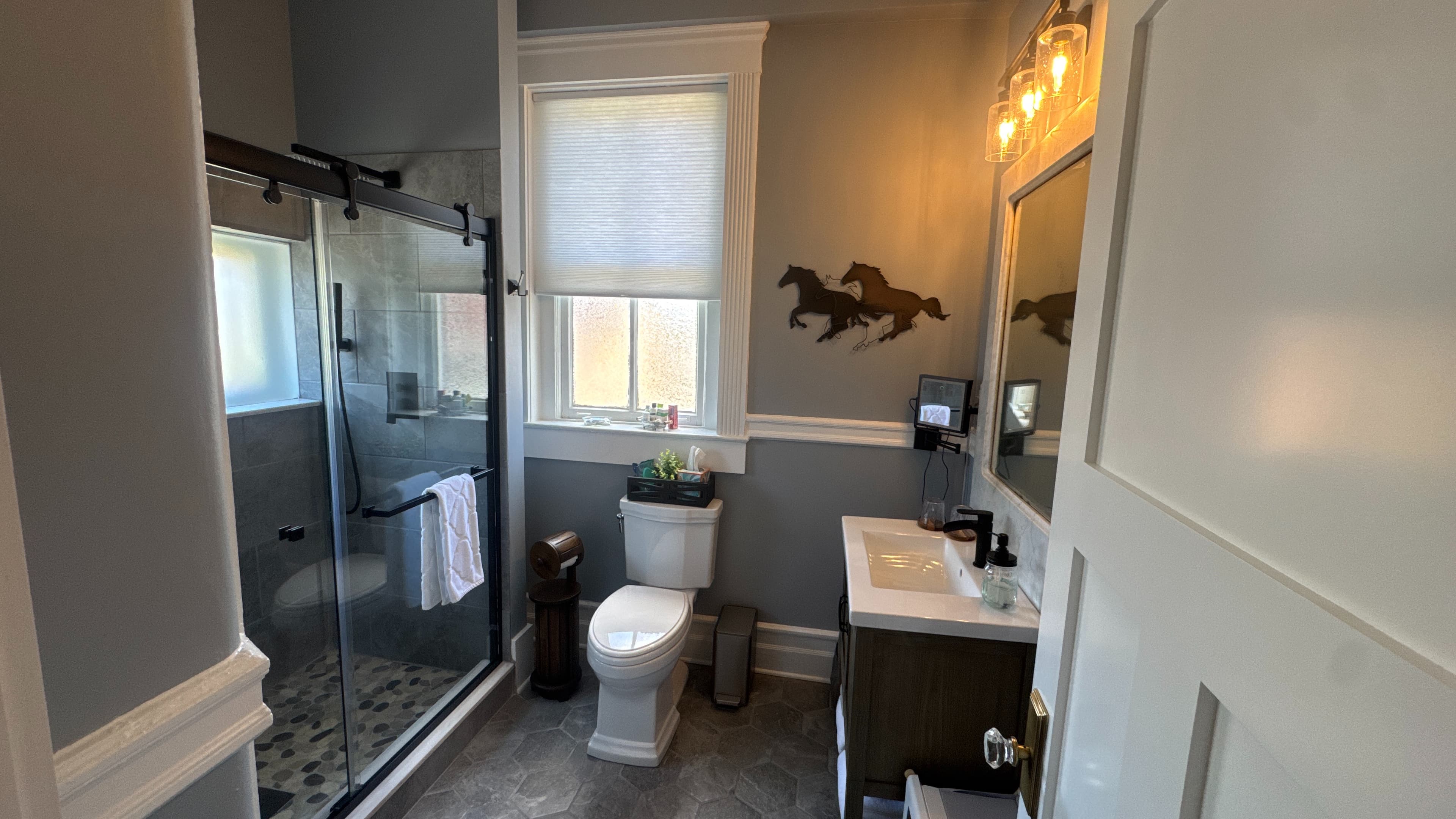 A doorway frames a view into a bathroom with a toilet, vanity, and horse artwork on the wall.