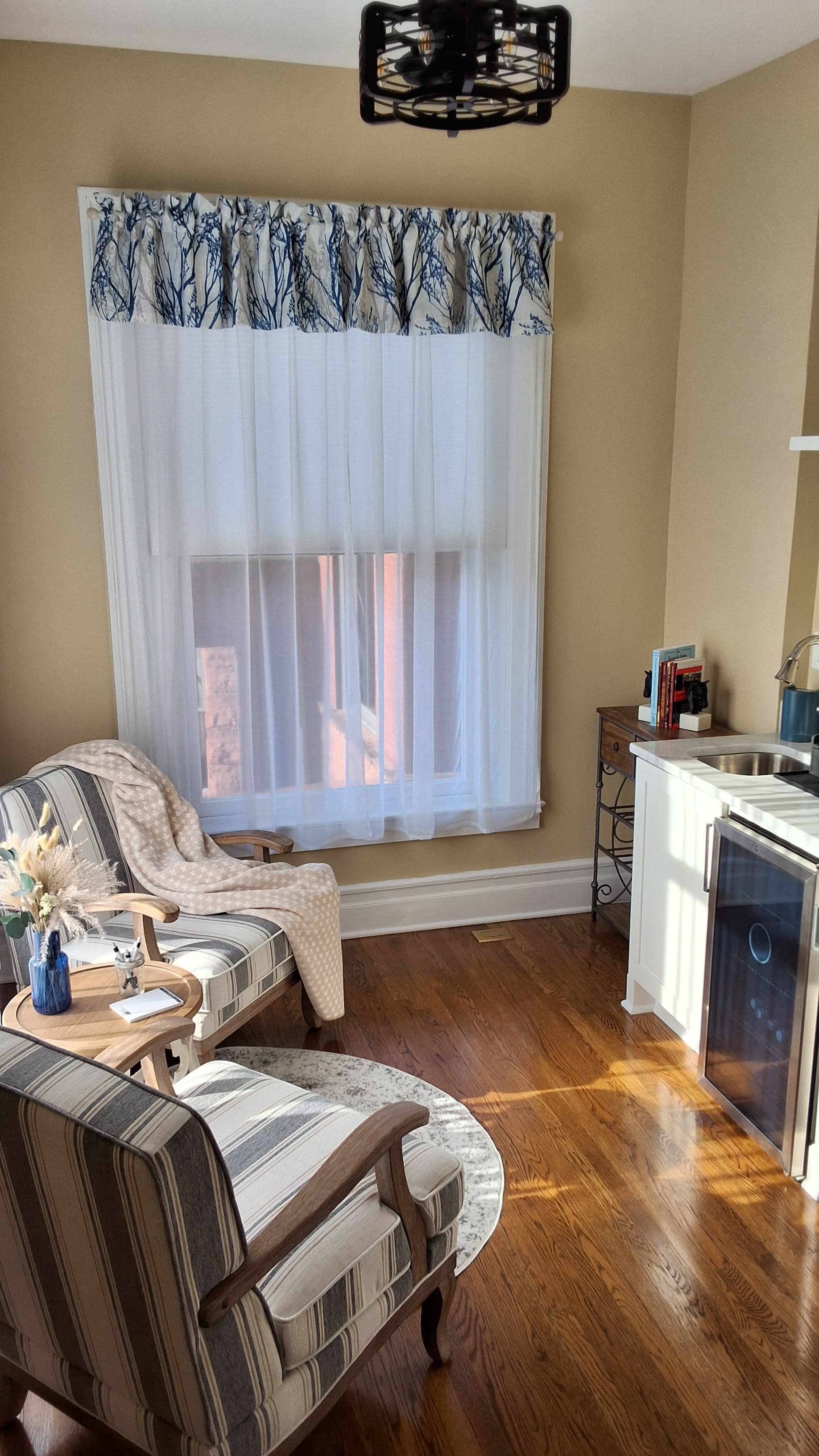 A cheerful sitting room with upholstered armchairs, hardwood floors, and windows letting in lots of natural light.