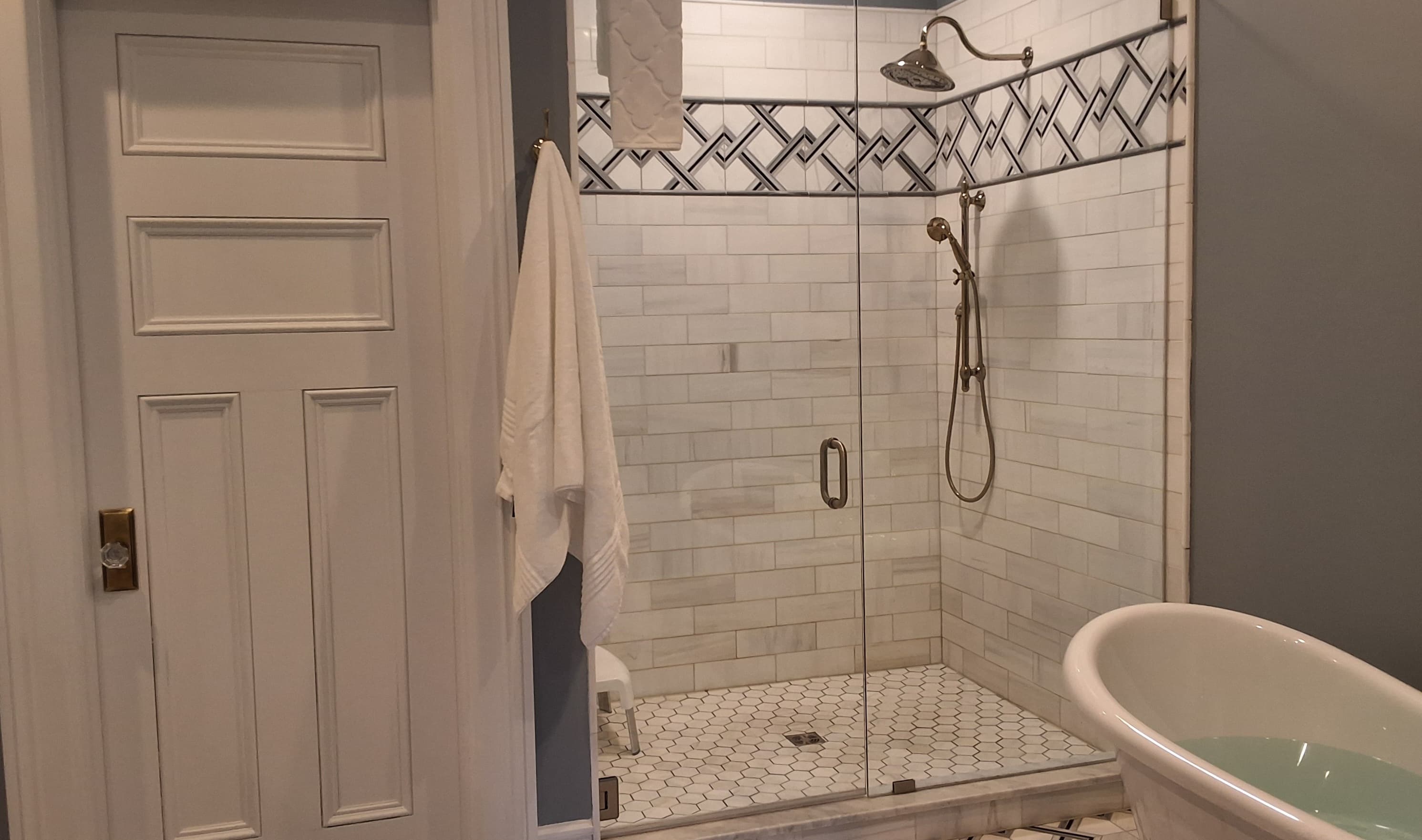 Spacious bathroom with glass-enclosed tiled shower and soaking slipper tub.