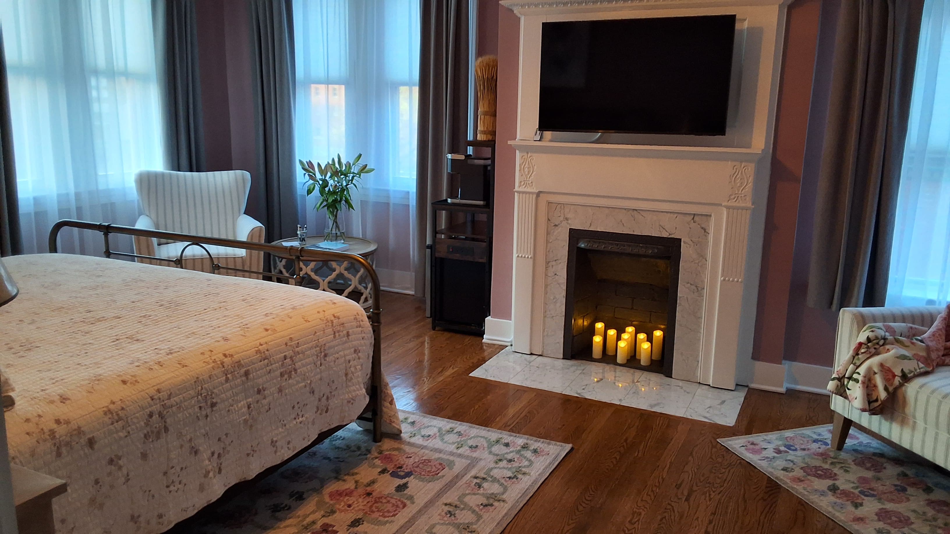 Charming bedroom with king-size bed, decorative fireplace, flat-screen TV, hardwood floors, and ceiling fan.