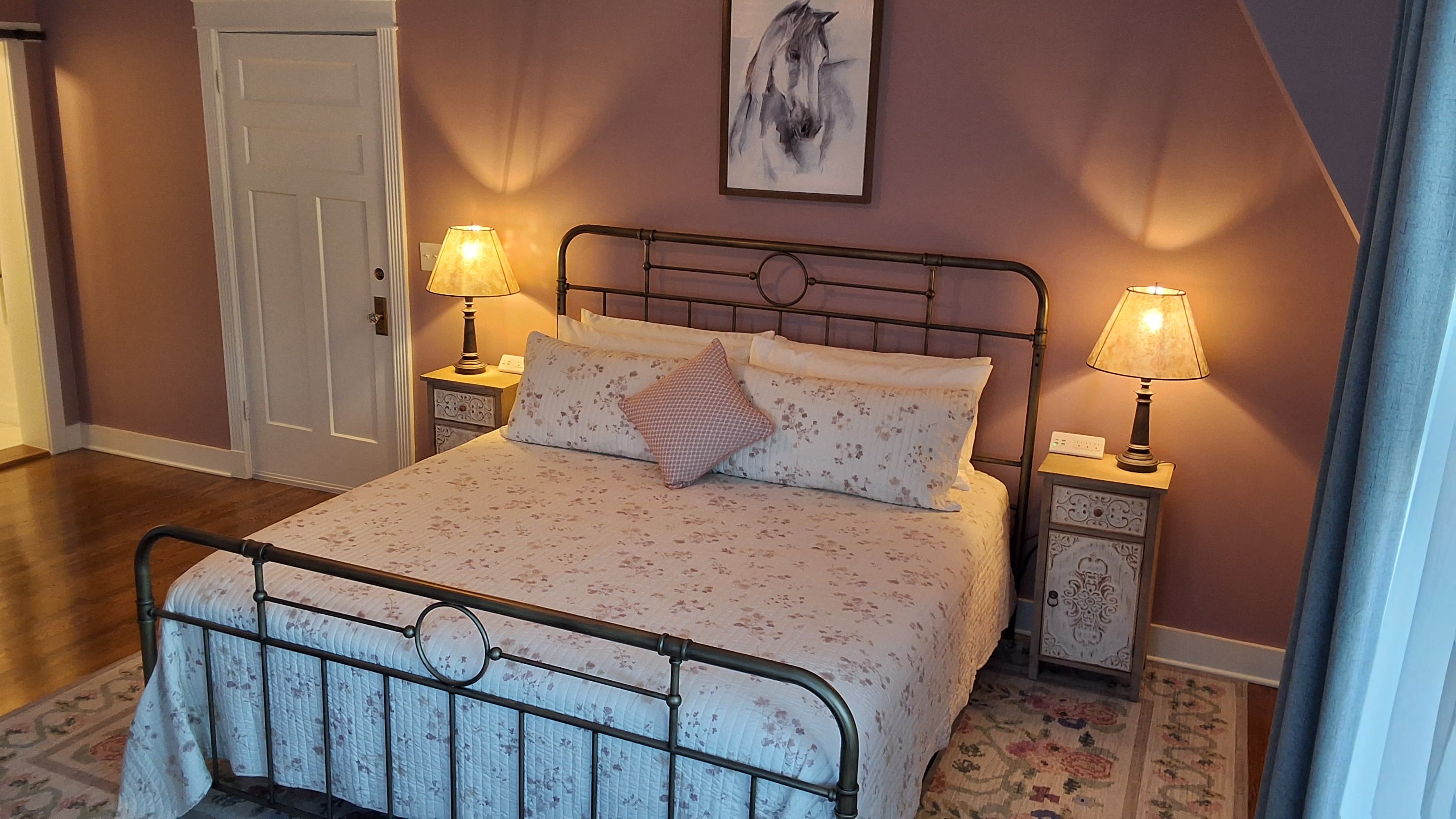 Romantic king-size metal bed with white and floral bedspread flanked by nightstands topped with matching lamps.