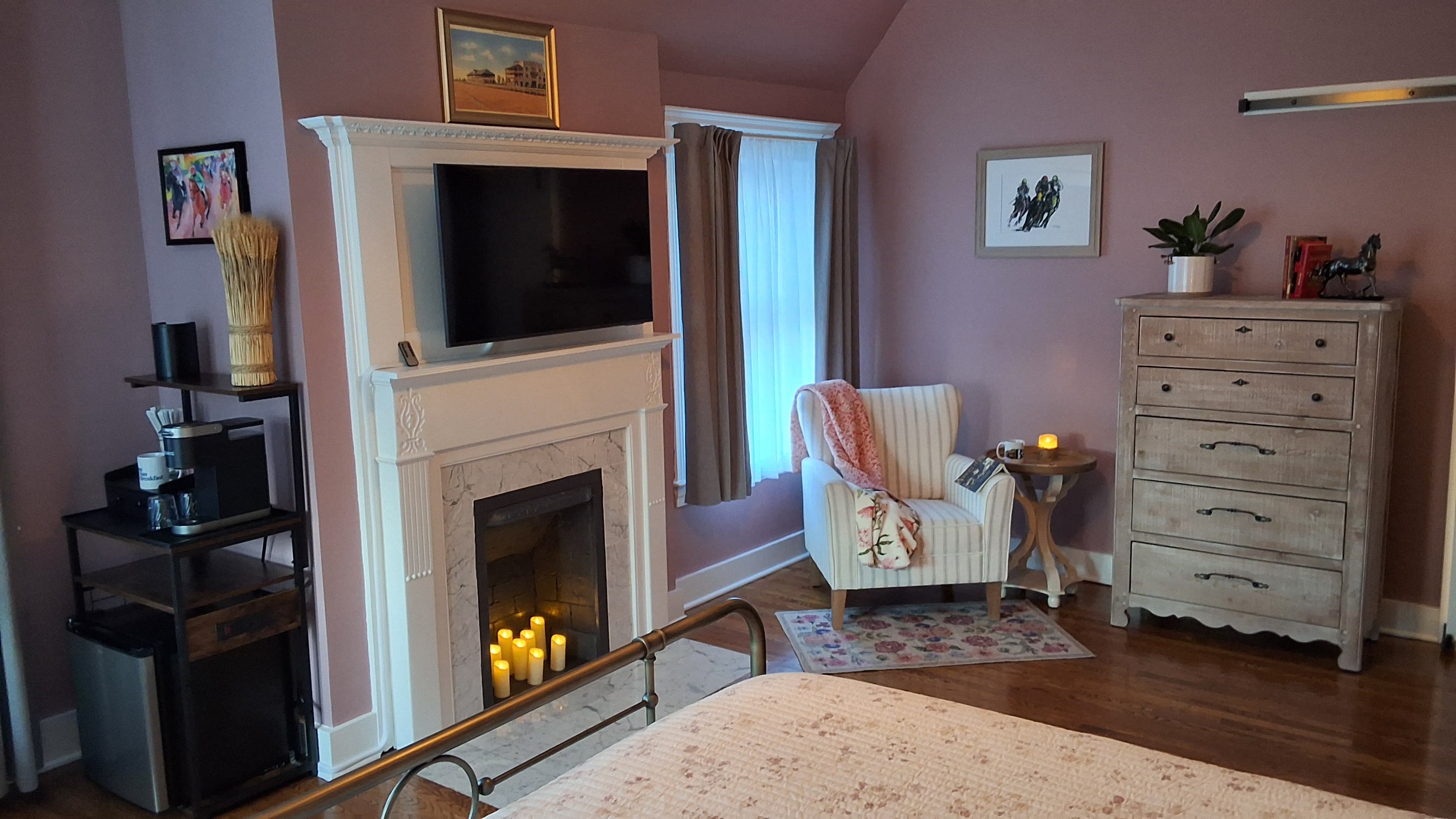 Romantic bedroom with king-size bed, decorative fireplace, flat-screen TV, wooden dresser, and coffee bar.