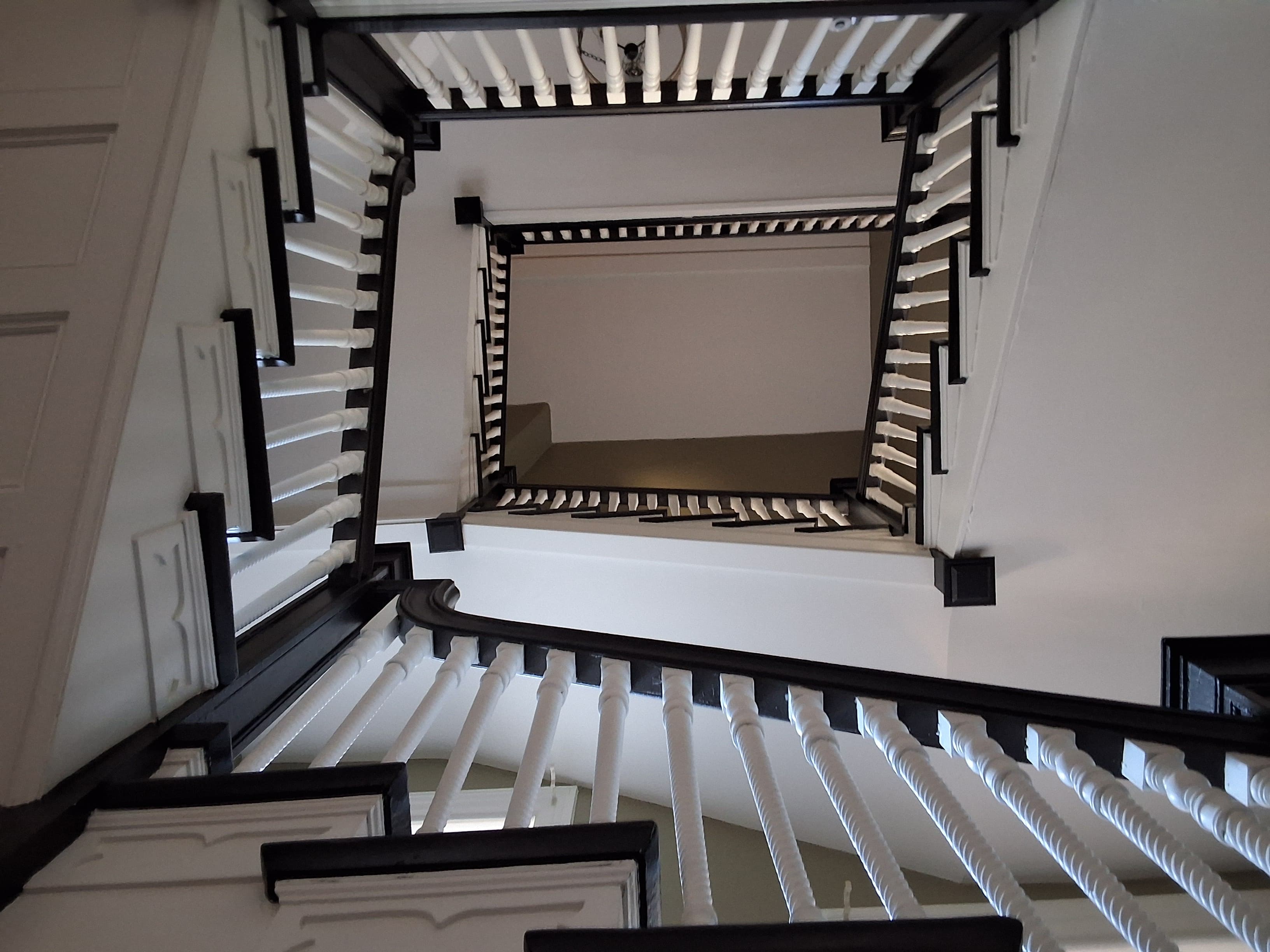 A view looking up a spiral staircase with white balustrades and black accents.