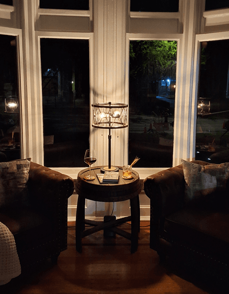 A cozy seating area with two armchairs, a lamp, and drinks on a small table, illuminated in the evening.