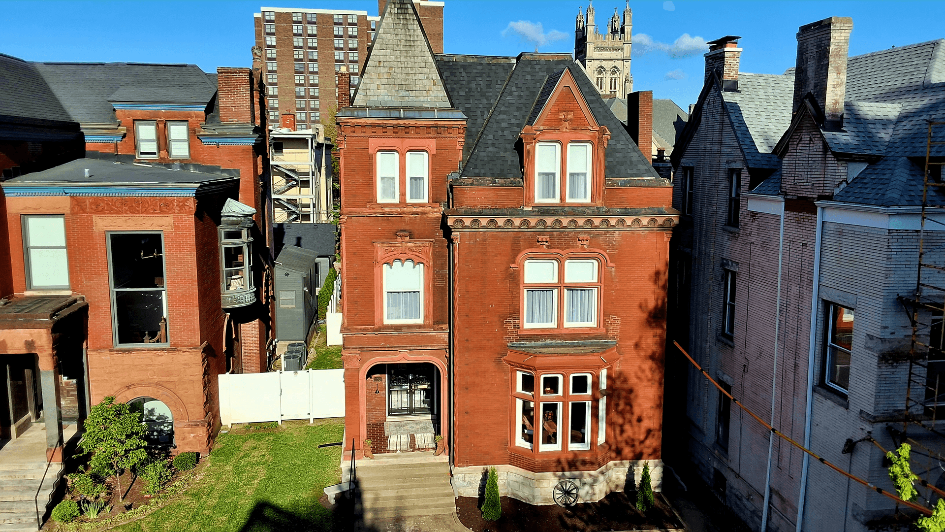 A historic red brick house surrounded by neighboring buildings and a clear blue sky.