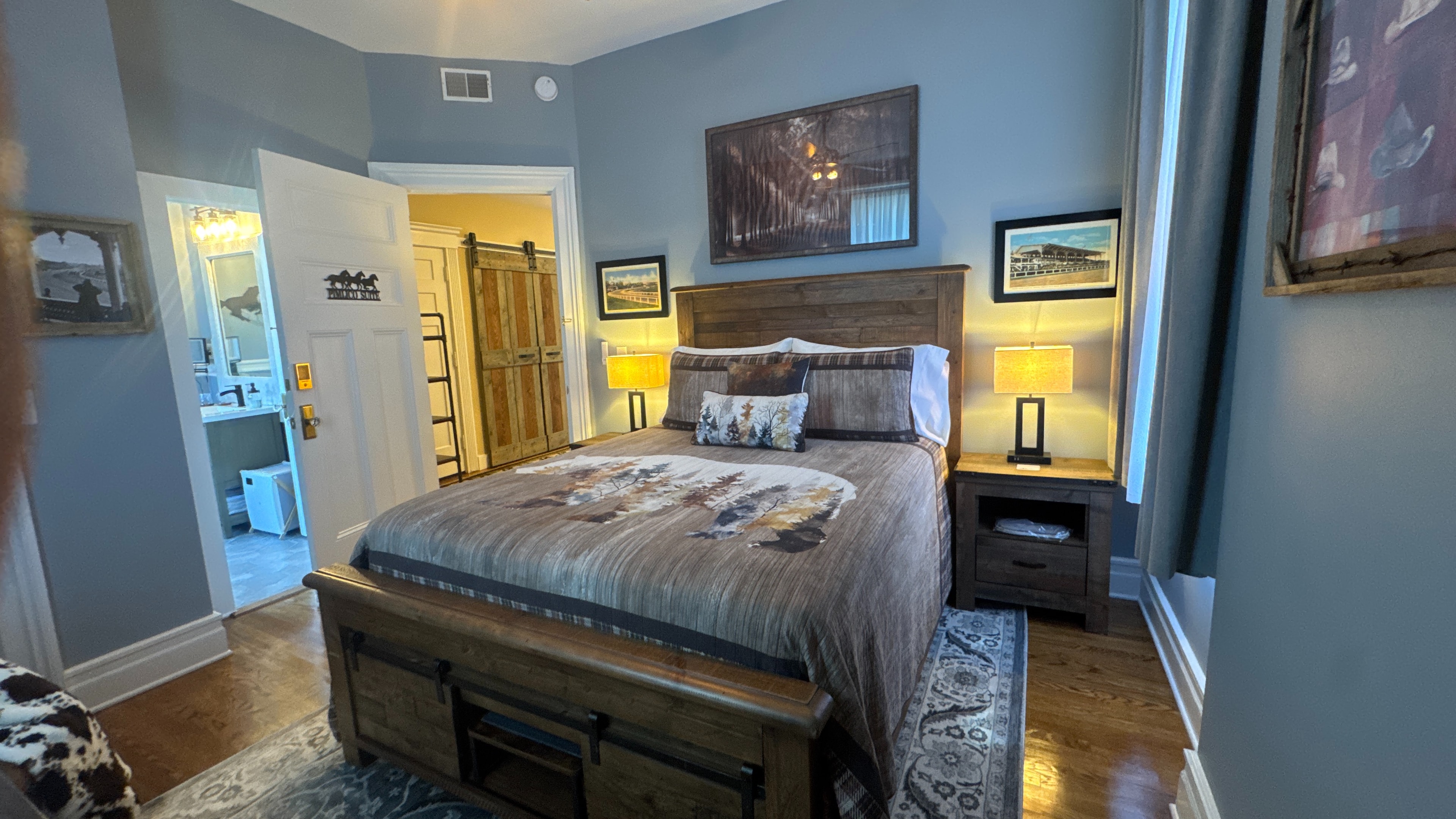 Cozy bedroom featuring a wooden bed with brown and plaid bedding, wooden nightstands with lamps, and framed artwork on gray walls.
