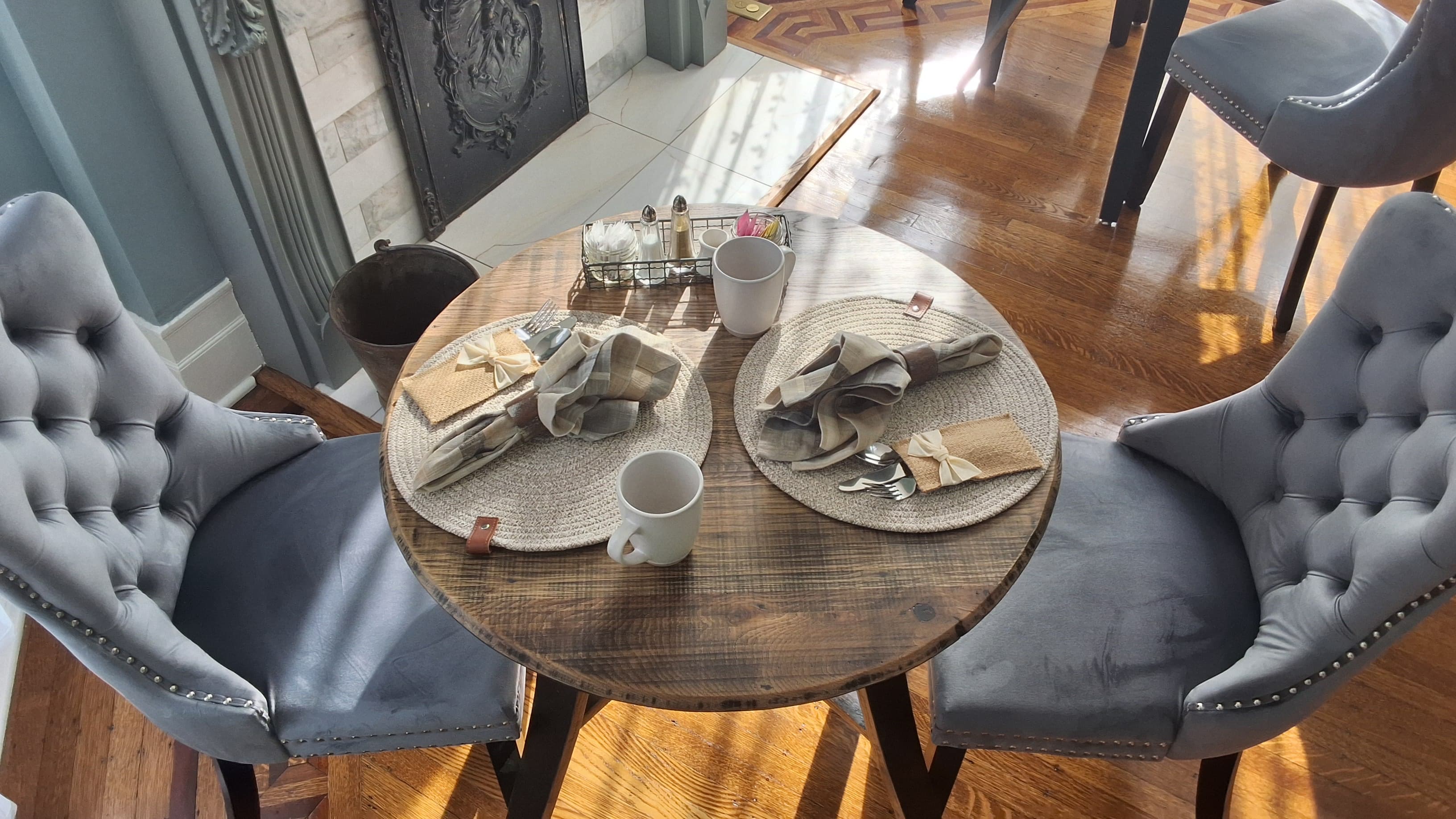 A cozy dining table set for two with elegant chairs, placemats, and coffee mugs.
