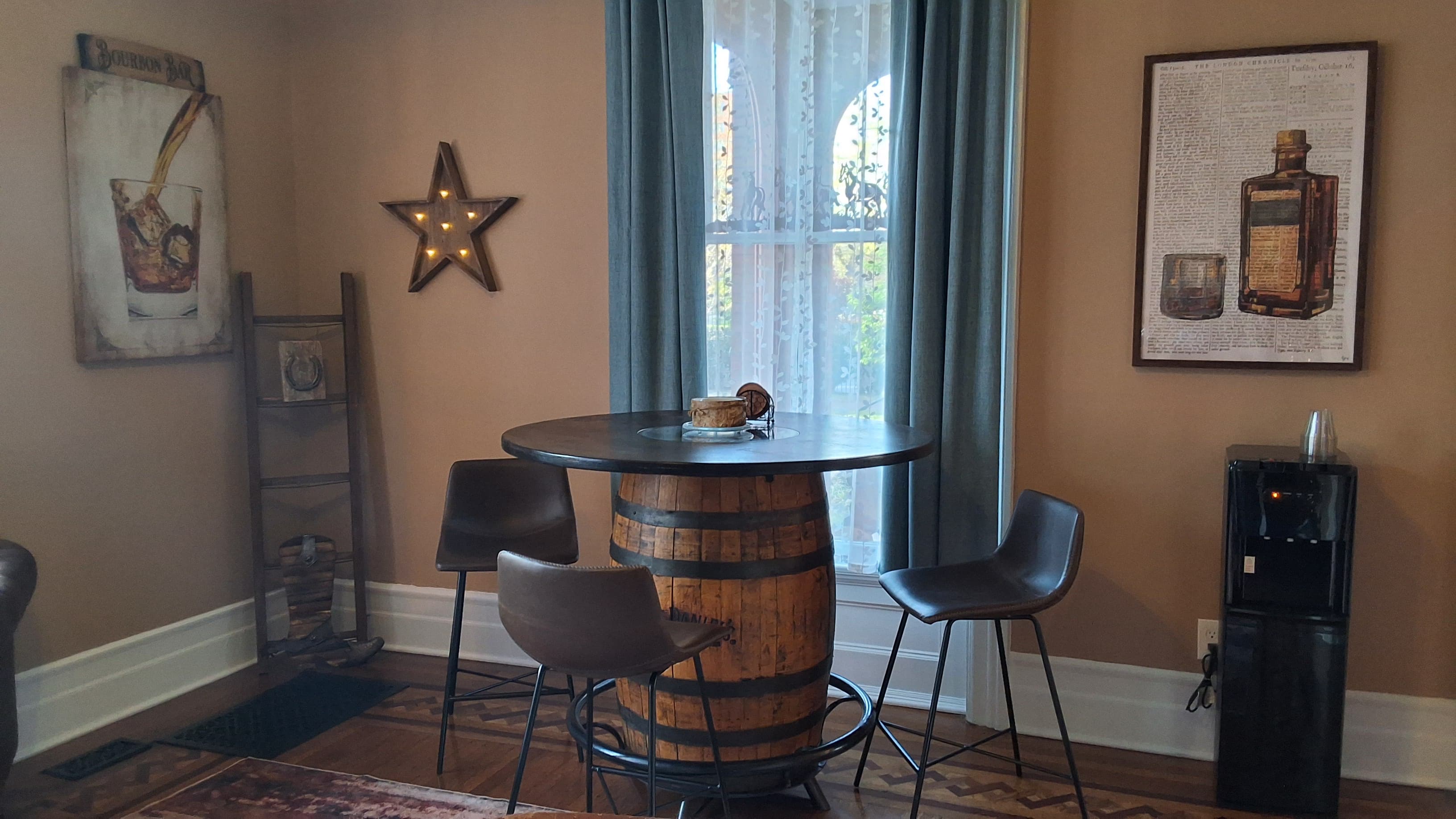 A cozy corner with a barrel-style table, two chairs, and a decorative wall featuring bourbon-themed artwork.