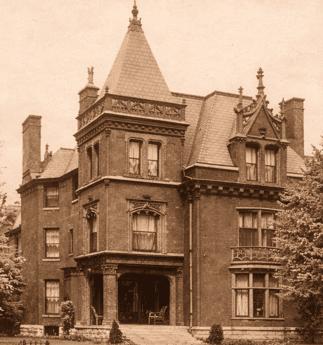 A vintage photograph of an ornate brick mansion with a steeply pitched roof and decorative features.