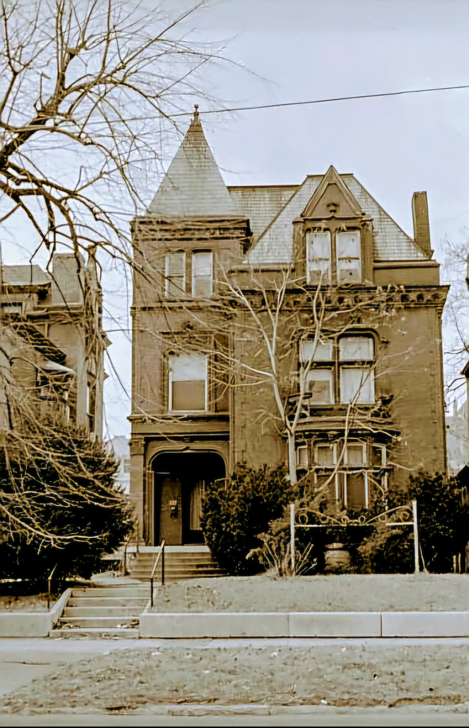 A Victorian-style house with a steep roof and ornate details, surrounded by bare trees.