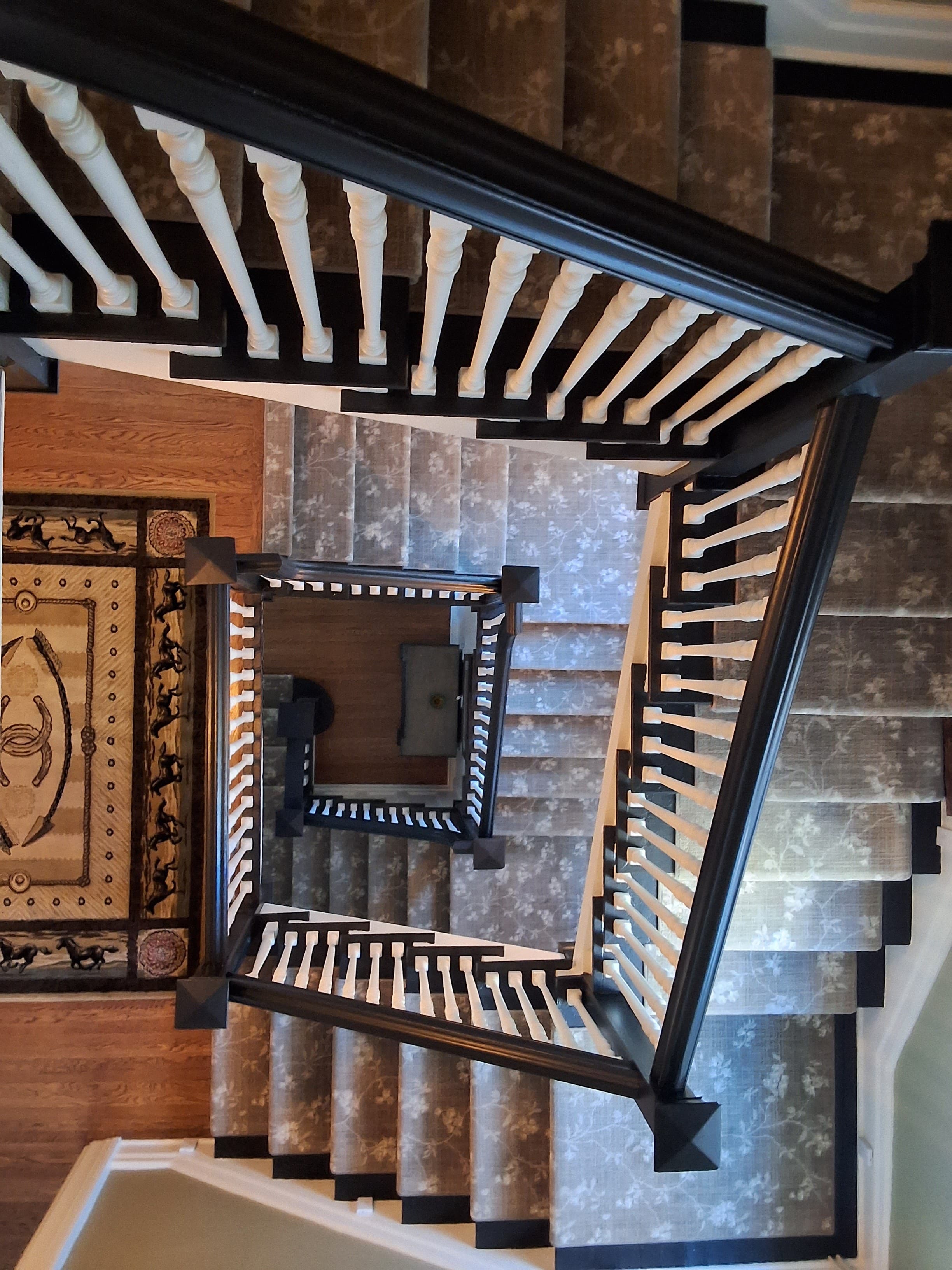 A view looking down a spiral staircase with decorative railings and a rug at the bottom.