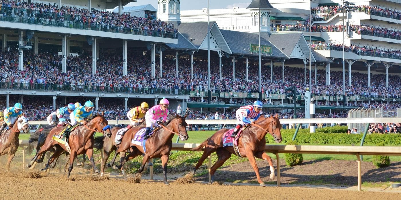 Horses race down the track at a crowded horse racing event.