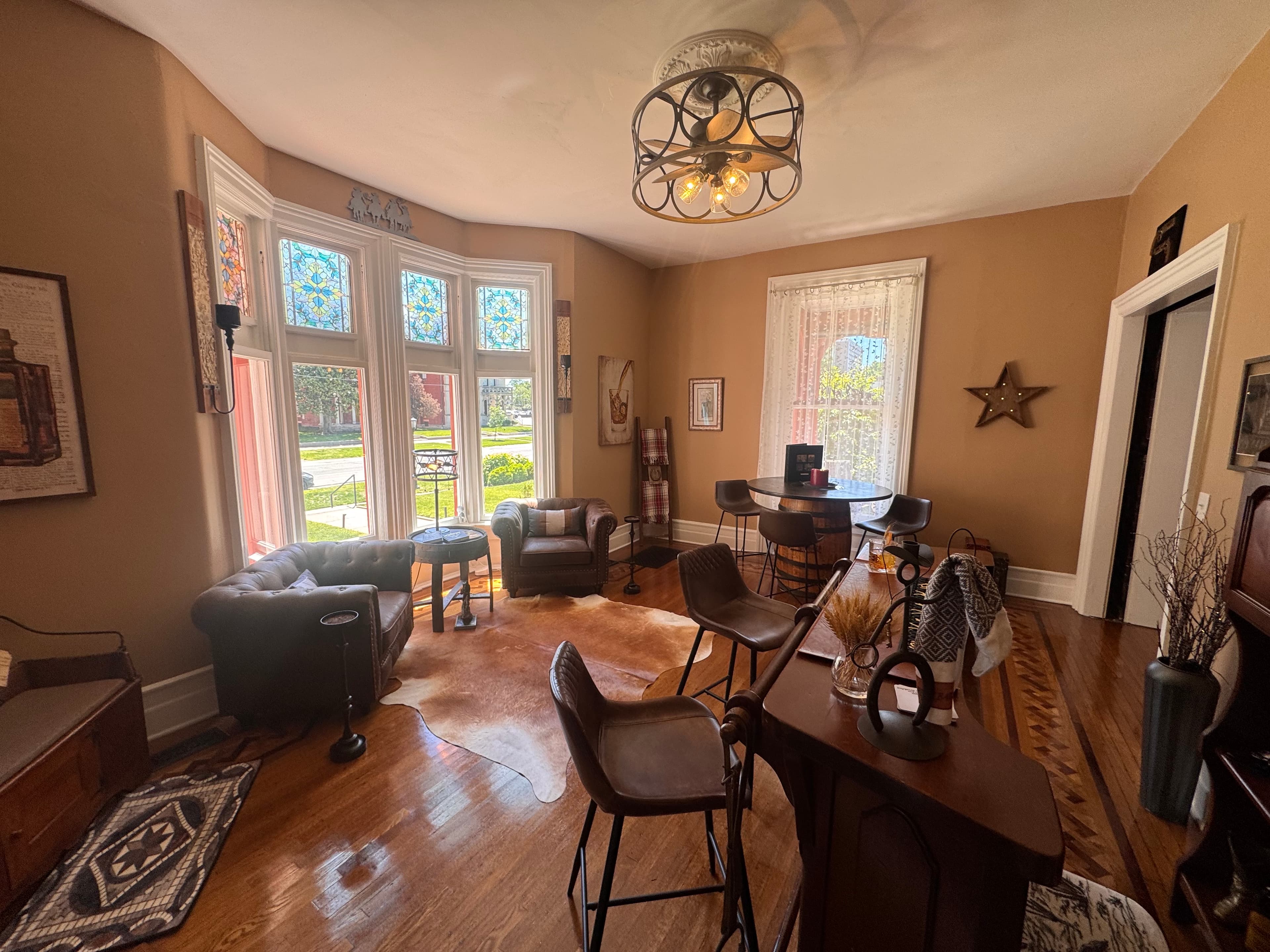 A cozy living room featuring a mix of vintage and modern furnishings, large windows, and decorative accents.