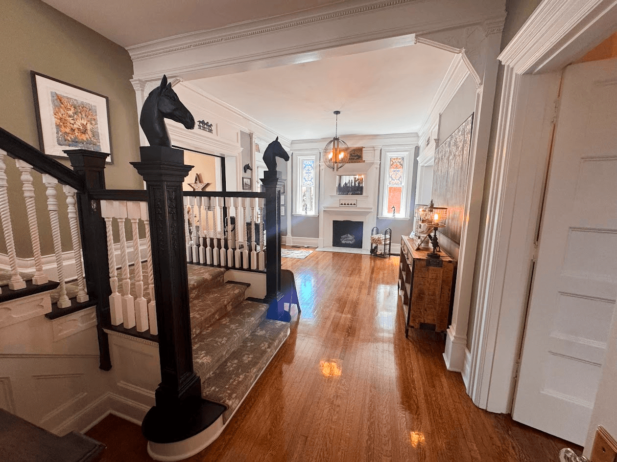 A spacious hallway with horse-head banisters, hardwood floors, and stained glass windows leads to a cozy living area.