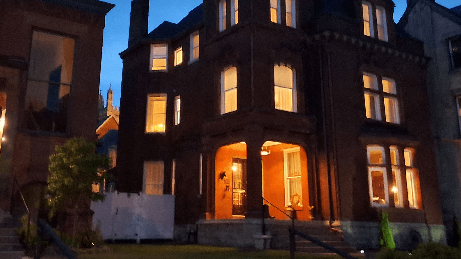 A two-story, brick Victorian house illuminated at dusk.