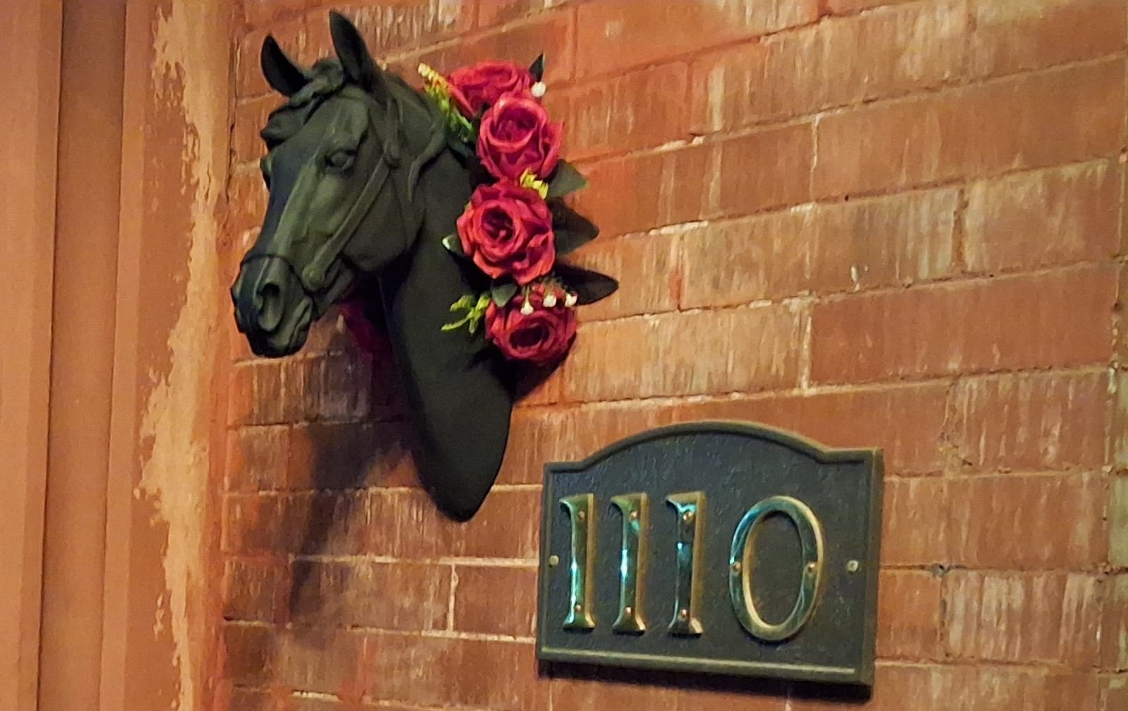 A decorative horse head with roses mounted on a brick wall near a door number plaque reading "1110."