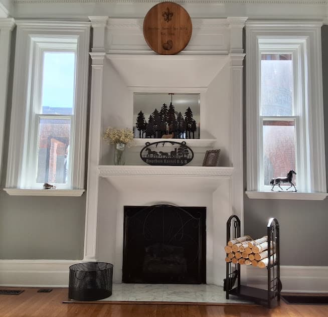 A cozy living room fireplace setup with decorative elements and natural light from two windows.