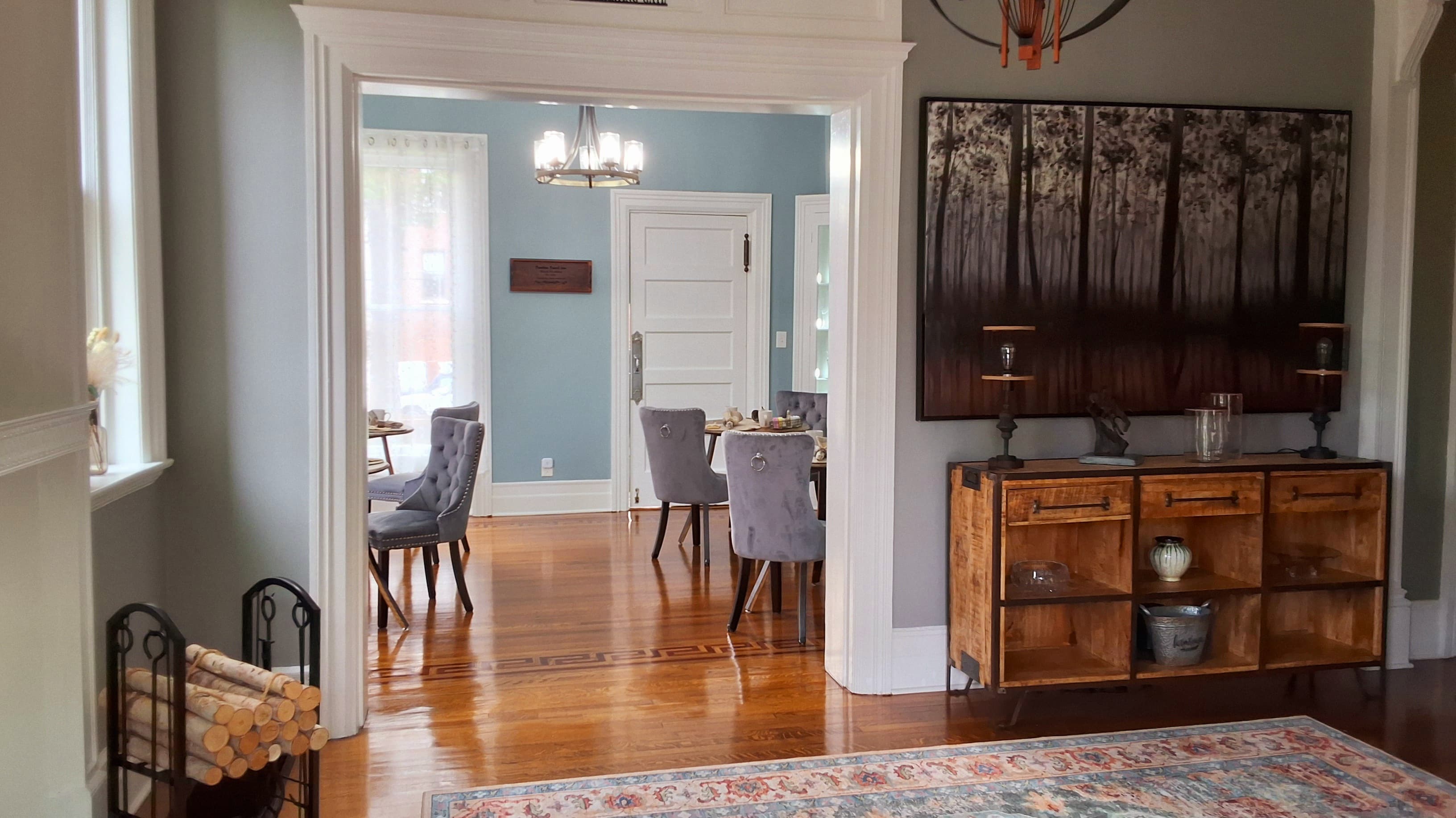 A view of a cozy dining area with elegant gray chairs and a wooden sideboard, framed by an archway in a well-lit room.