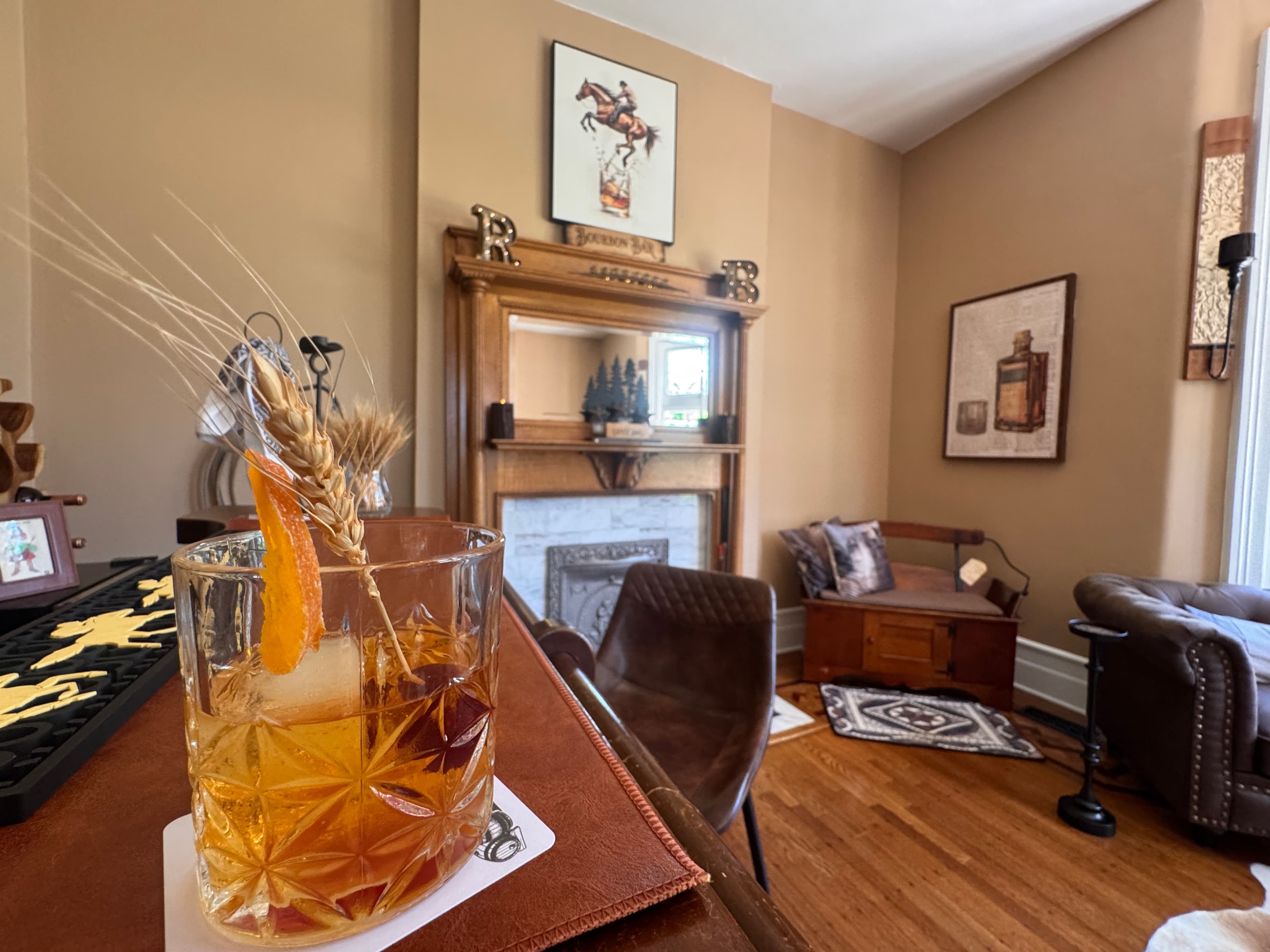 A close-up of an elegantly garnished cocktail on a bar, with a cozy room setting in the background.