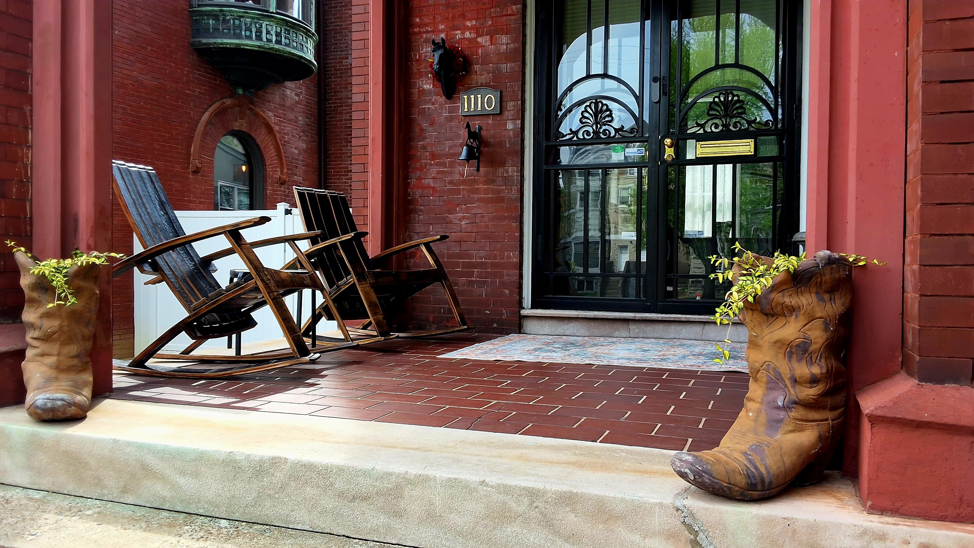 A porch features wooden rocking chairs and two planters shaped like cowboy boots.