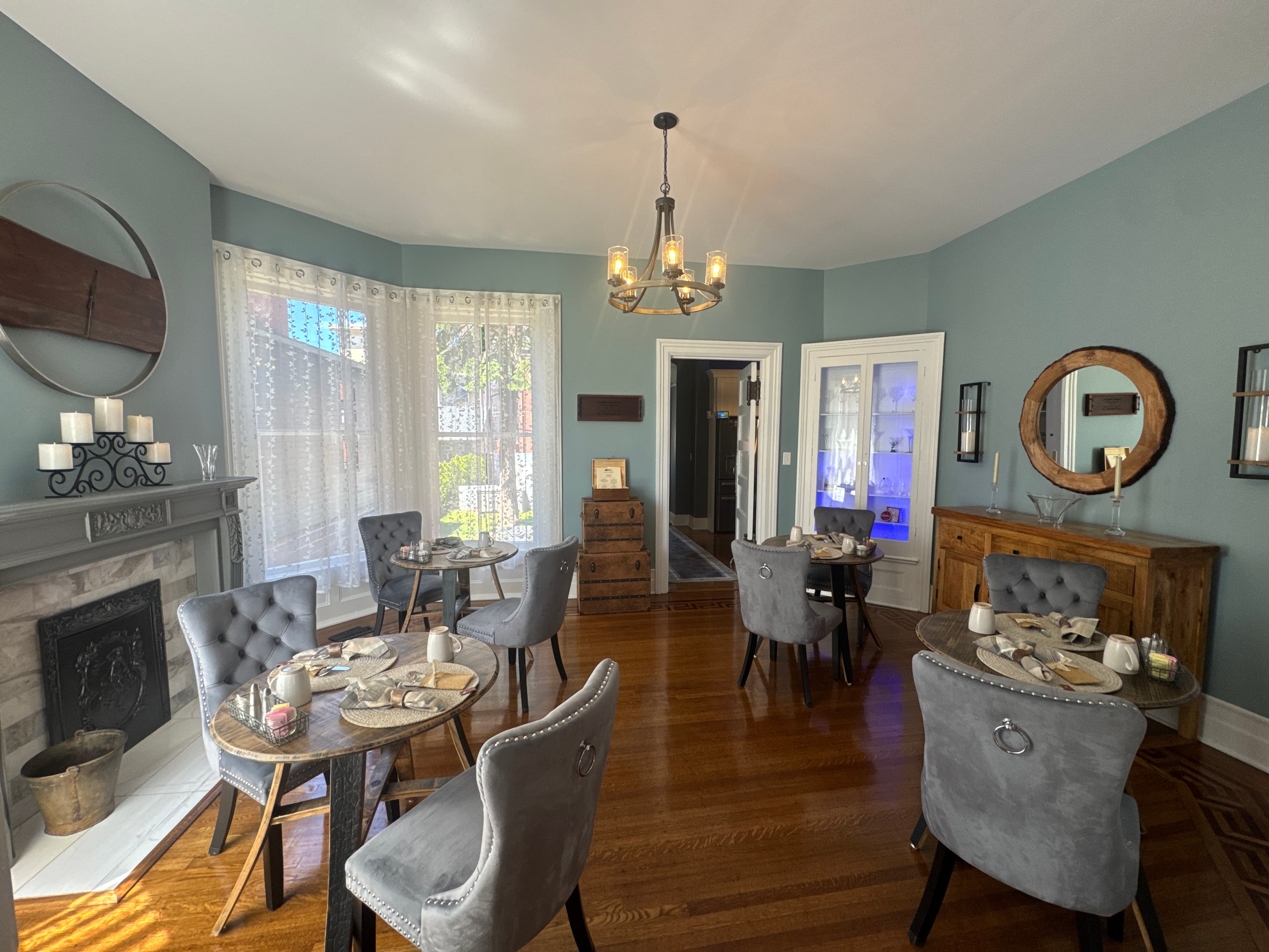 A stylish dining room featuring round tables with grey chairs, elegantly set for a meal, and a cozy ambiance adorned with soft lighting and decor.